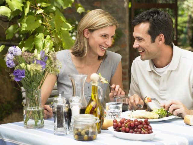 Couple en train de déjeuner à la table en plein air avec de la salade sur les assiettes.